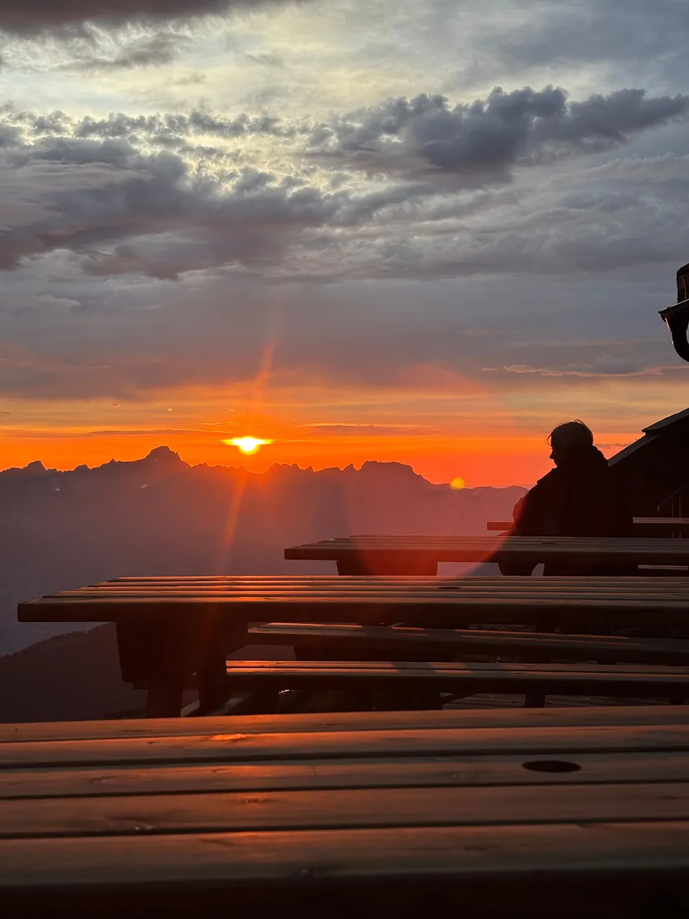 Coucher de soleil sur les montagnes depuis la terrasse du refuge, une personne attablée face à l'horizon